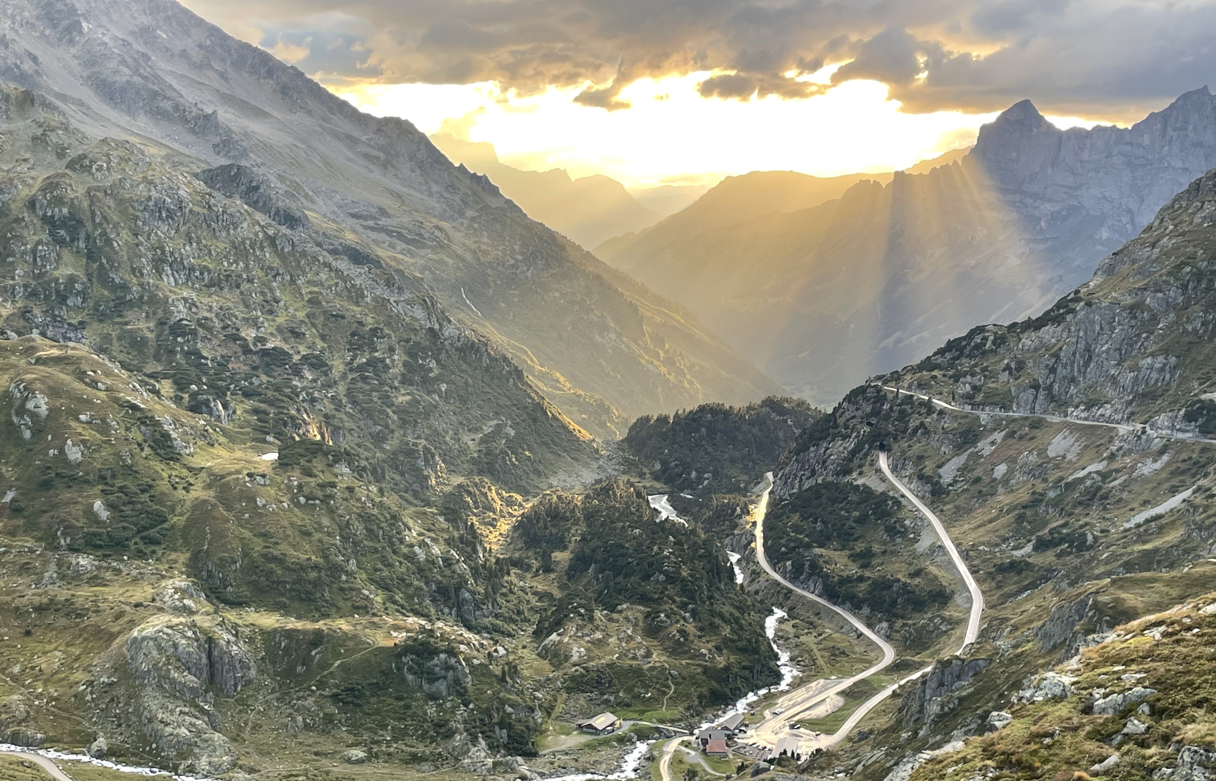 Sunbeams over a mountain valley and a winding Alpine road