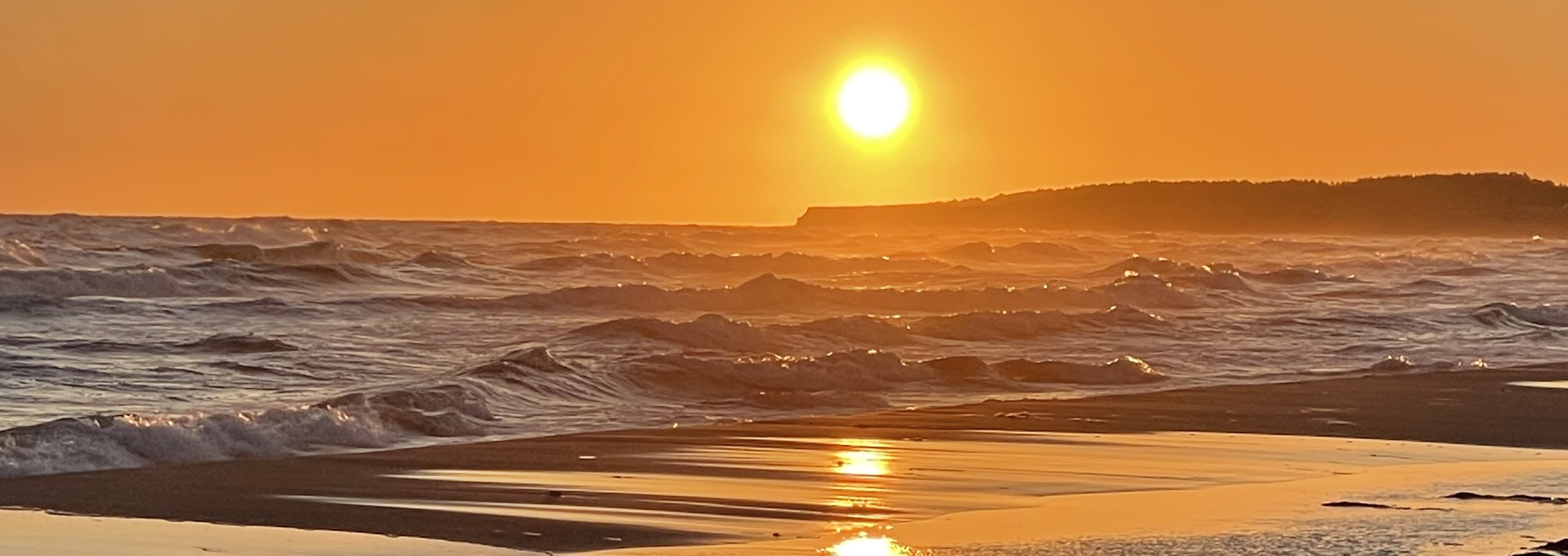 A golden sunset over ocean waves reflected in wet sand along the shore
